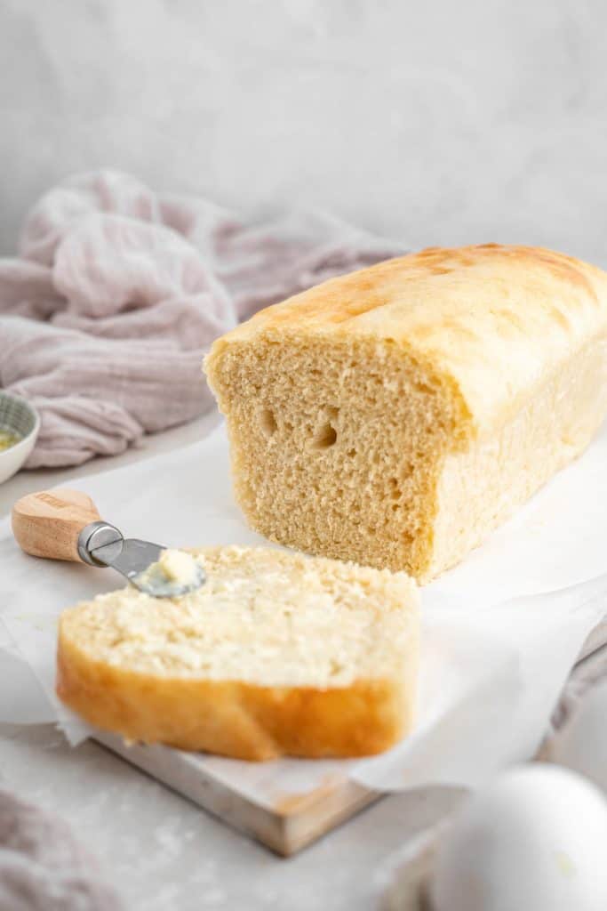 A loaf of bread resting on parchment paper with a towel in the background