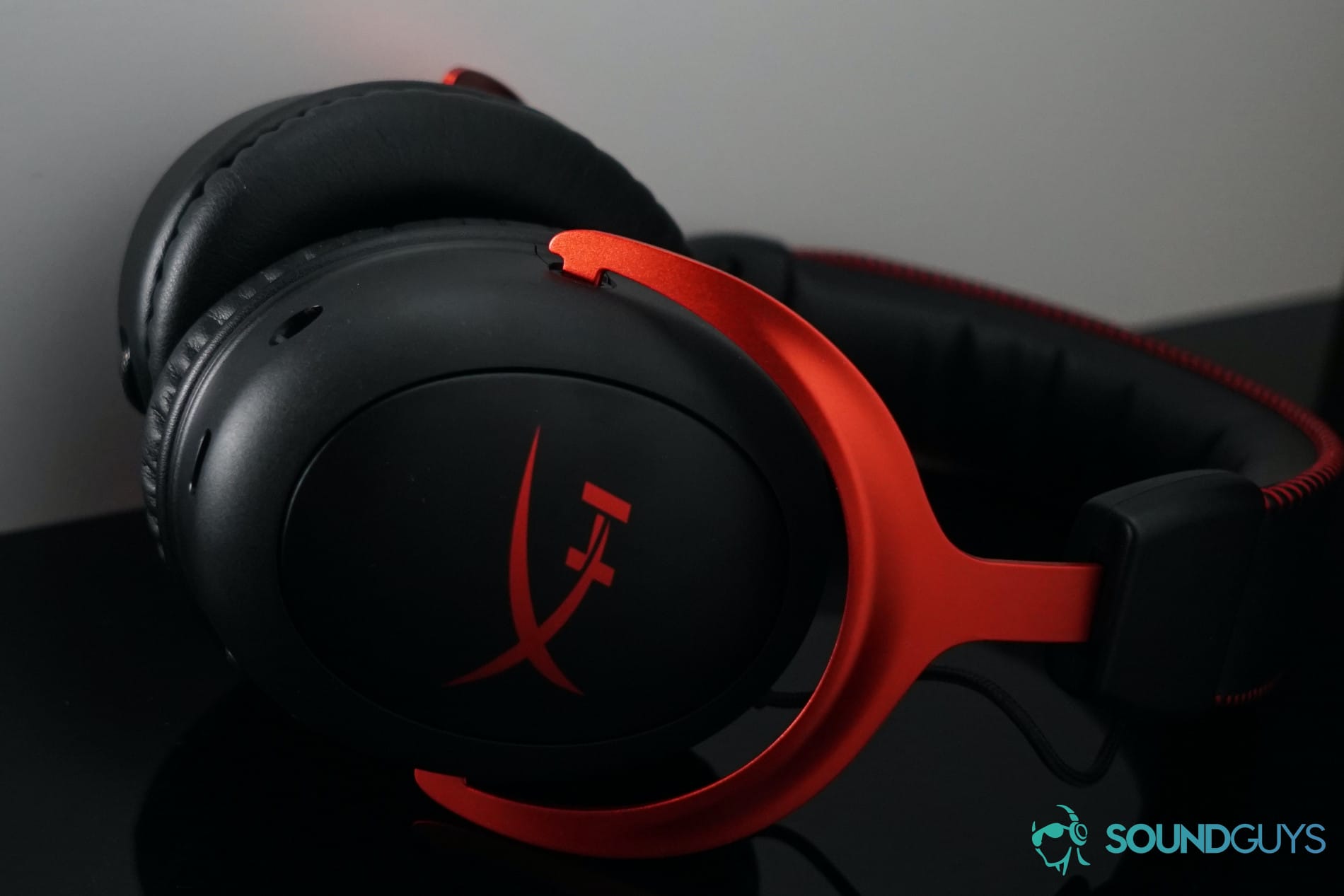 The HyperX Cloud II Wireless lays on a black reflective surface on a white shelf with its mic detached.