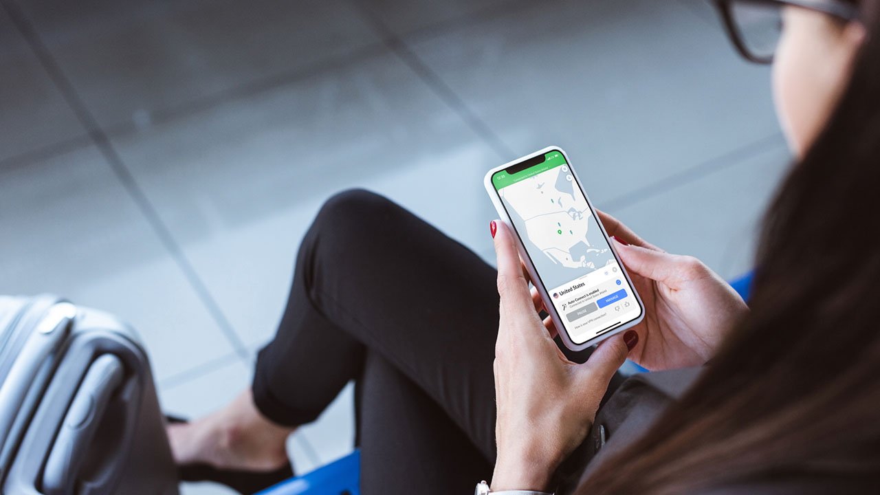 Person using smartphone displaying a map of NordVPN server locations, sitting next to a suitcase in an airport setting.